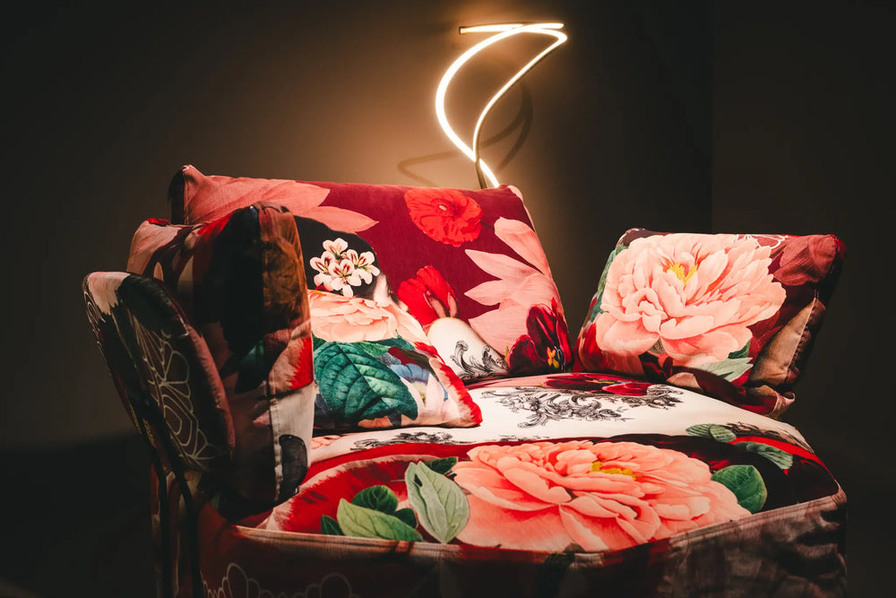 Sessel mit floralem Rosenmuster-Bezug und dekorativen Kissen unter geschwungener Neon-Wandleuchte – Wohnzimmermöbel Möbel Graf Dresden
