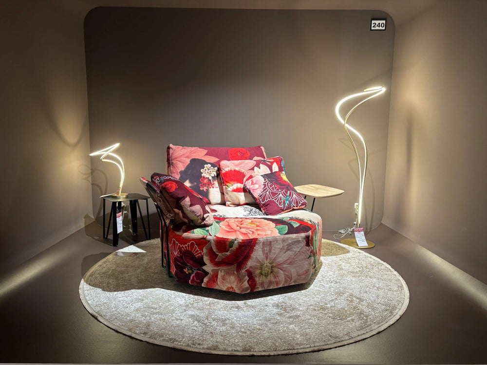 Polstermöbel Dresden – Floraler Drehsessel mit buntem Blumenmuster und Neon-Stehleuchte in dunkler Showroom-Nische, Möbel Graf