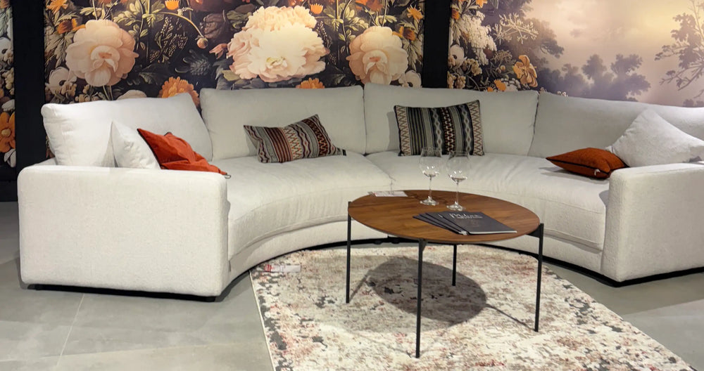 Weißes Rundsofa vor Blumentapete mit passenden Kissen in Weiß, Orange und Braun in der Ausstellung – Wohnzimmermöbel im Möbelhaus bei Heidenau