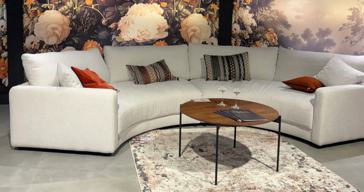 Weißes Rundsofa vor Blumentapete mit passenden Kissen in Weiß, Orange und Braun in der Ausstellung – Wohnzimmermöbel im Möbelhaus bei Heidenau